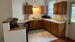A compact kitchen with wooden cabinets, a built-in sink, and a window with blinds.