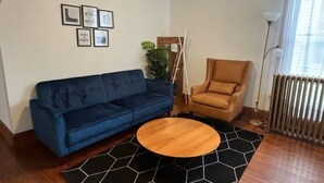A living room with a blue sofa, a brown armchair, a round wooden coffee table, and a black rug with white hexagonal patterns.