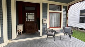 A covered porch with a wooden door, a small table, two chairs, and a mailbox.