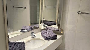 Un bagno moderno con uno specchio grande, un lavandino bianco e uno spazio doccia.