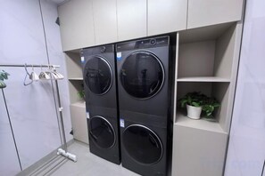 A laundry area with two front-loading washing machines, a drying rack, and a shelf with a potted plant. - Renhe Hotel (Heihe)