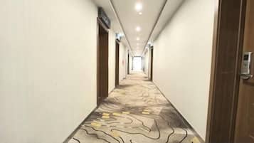 A hotel corridor with a patterned carpet, doors on both sides, and a ceiling with recessed lighting.