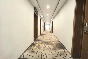 Pasillo de hotel con alfombra estampada, puertas a ambos lados y techo con iluminación empotrada.