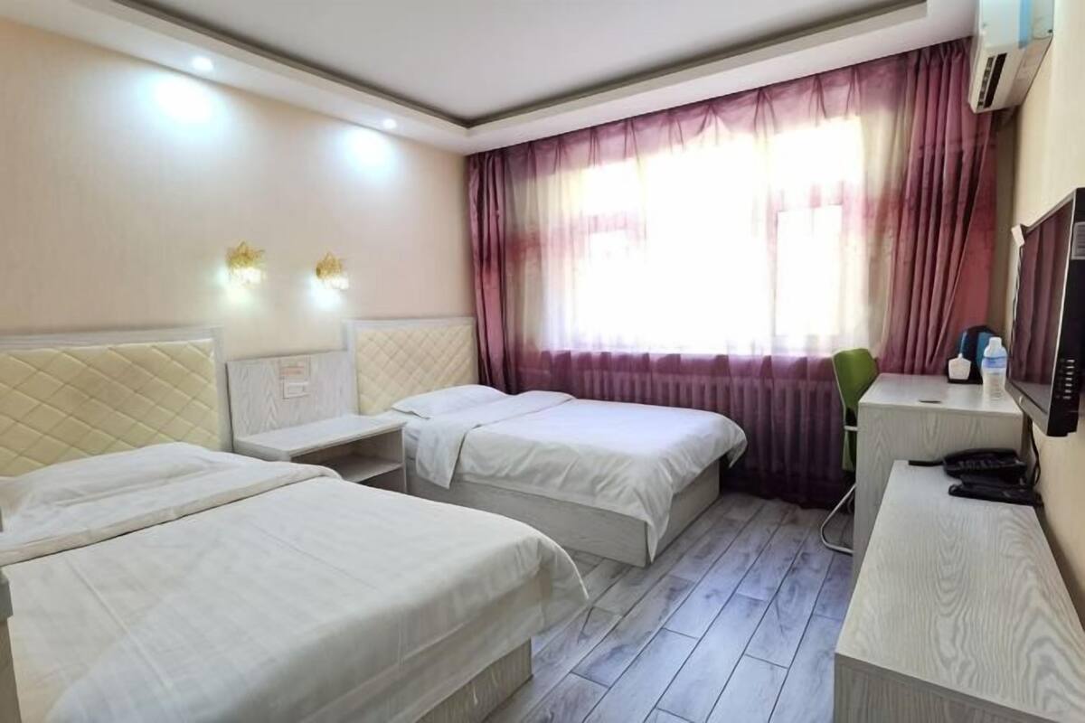 Ein Hotelzimmer mit zwei Betten, einem Schreibtisch, einem Stuhl, einem Fernseher und einem Fenster mit Vorhängen.
