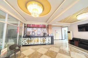 A hotel reception area with a check-in counter, a chandelier, a reception desk, and a seating area.