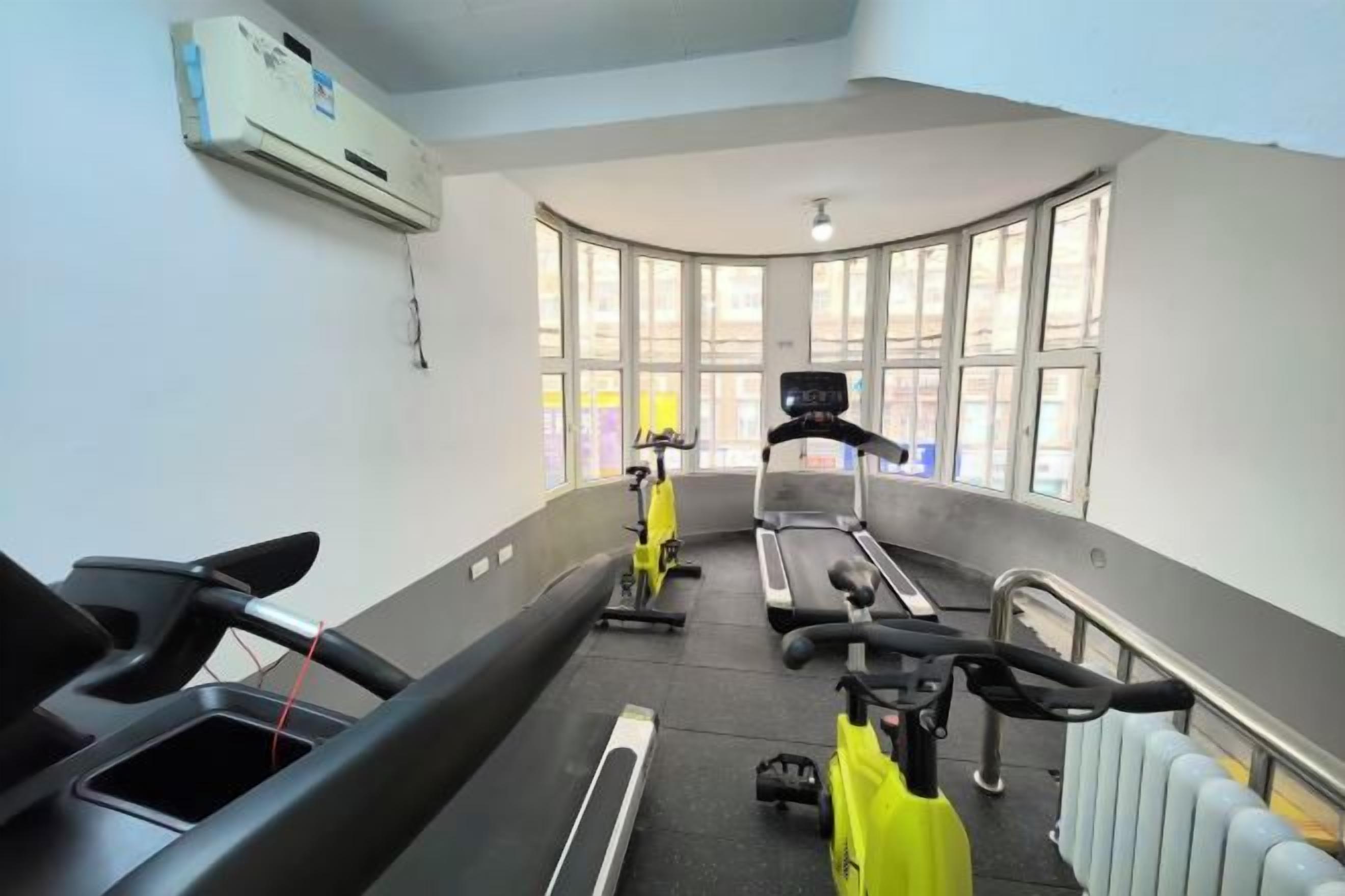 Un gimnasio con equipo de ejercicio, ventanas amplias y un radiador.