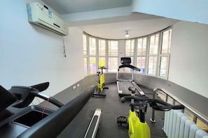 A gym with exercise equipment, large windows, and a radiator. - Renhe Hotel (Heihe)