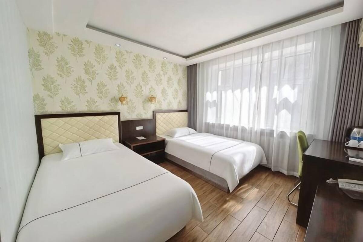 Ein Hotelzimmer mit zwei Betten, einem Schreibtisch und einem Fenster mit Vorhängen.