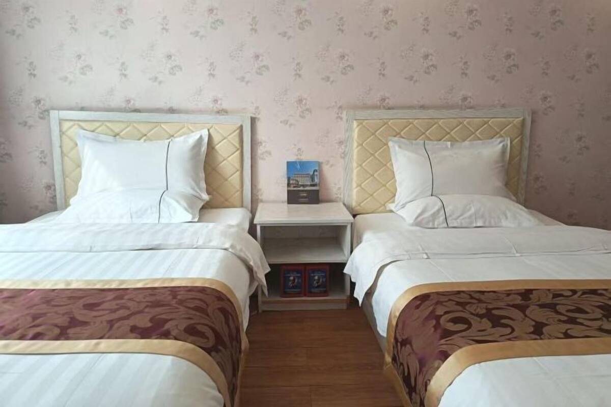 Ein Hotelzimmer mit zwei Betten, einem Nachttisch und einer kleinen Regalanlage mit Büchern.