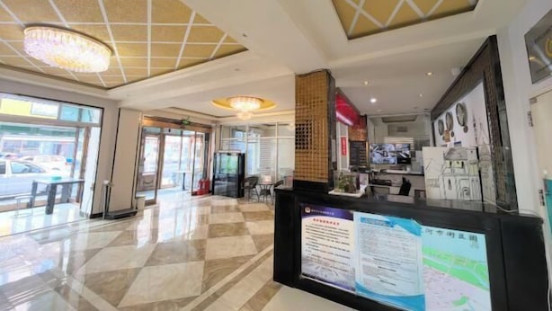 Un vestíbulo de hotel con piso a cuadros, una recepción con carteles informativos y una araña.