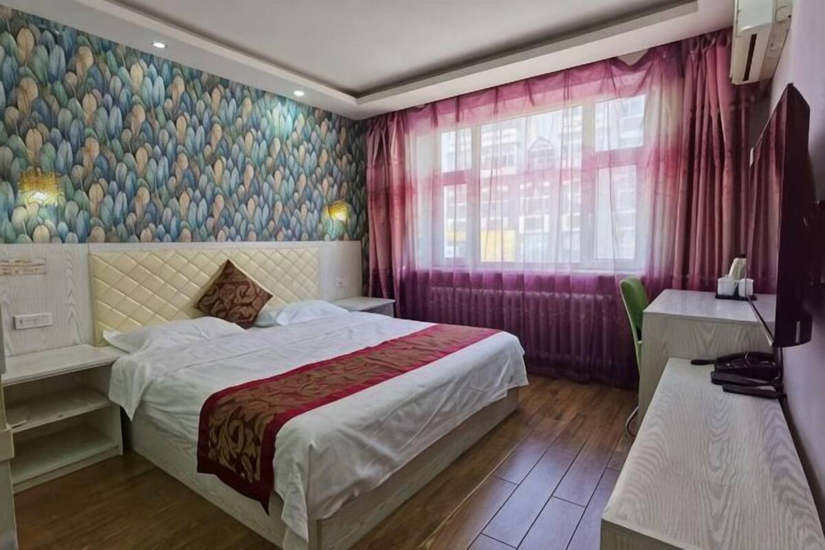Ein Hotelzimmer mit Bett, Nachttischen, Schreibtisch, Sessel und Fernseher, sowie einem Fenster mit Vorhängen.