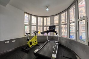 A gym with a treadmill and a stationary bike, large windows, and a ceiling light. - Renhe Hotel (Heihe)