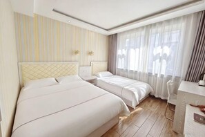 Hotellihuone, jossa on kaksi sänkyä, työpöytä ja suuri ikkuna, jossa on verhot.