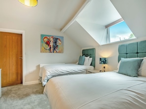 A bedroom with two beds, a wooden door, a painting, and a skylight.