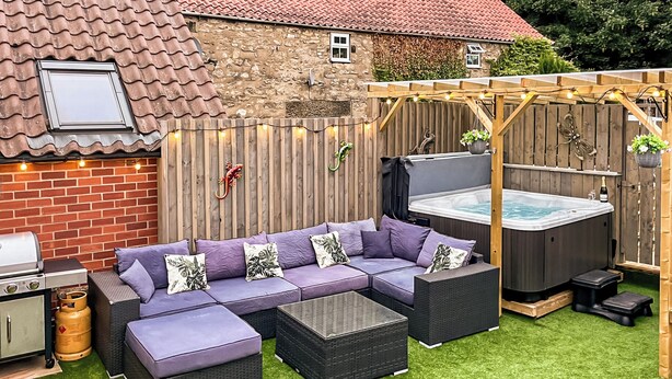Un jardin avec un canapé d’angle, un jacuzzi et un barbecue.