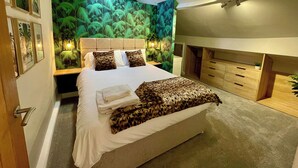 Une chambre à coucher moderne avec un grand lit, une tête de lit dotée d’un éclairage intégré, une commode en bois et une fresque murale sur le thème des tropiques.