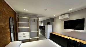 A modern bedroom with a bed, a wardrobe, a desk, a television, and a kitchen area. - MOVE (João Pessoa)