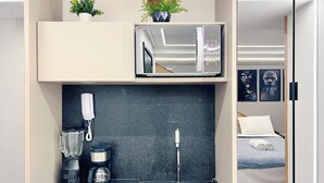 A modern hotel room with a kitchenette, a coffee maker, a blender, a sink, and a bed with a rolled-up towel. - MOVE (João Pessoa)