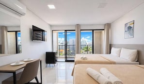 Une chambre d’hôtel avec deux lits, un bureau, une chaise, une télévision et un balcon donnant sur la ville.