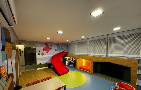 A children's play area with a slide, seating, and a fireplace. - MOVE (João Pessoa)