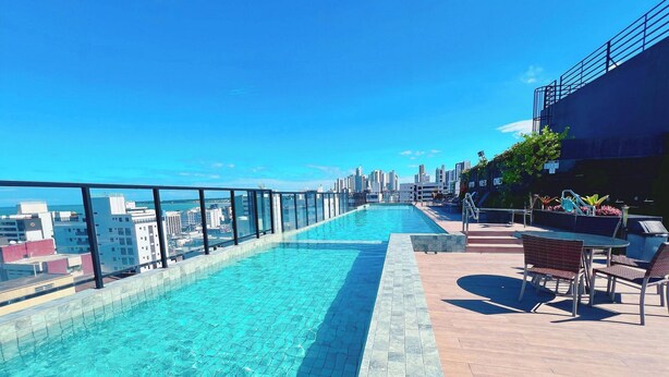 A rooftop pool with a city view, a seating area with chairs, and a railing. - MOVE (João Pessoa)