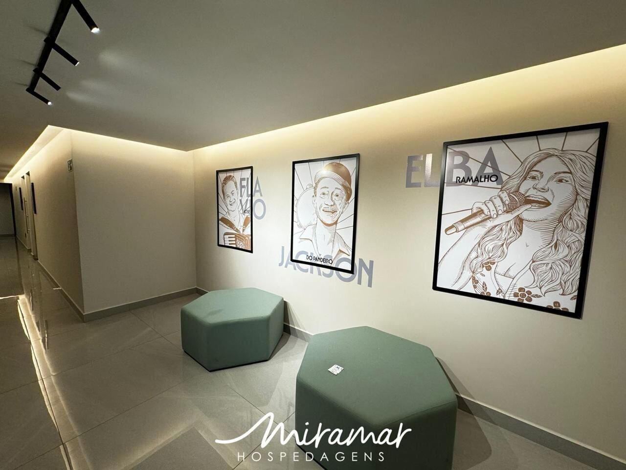 A hallway with framed artwork on the walls, a seating area with green cushions, and a clean, modern design.