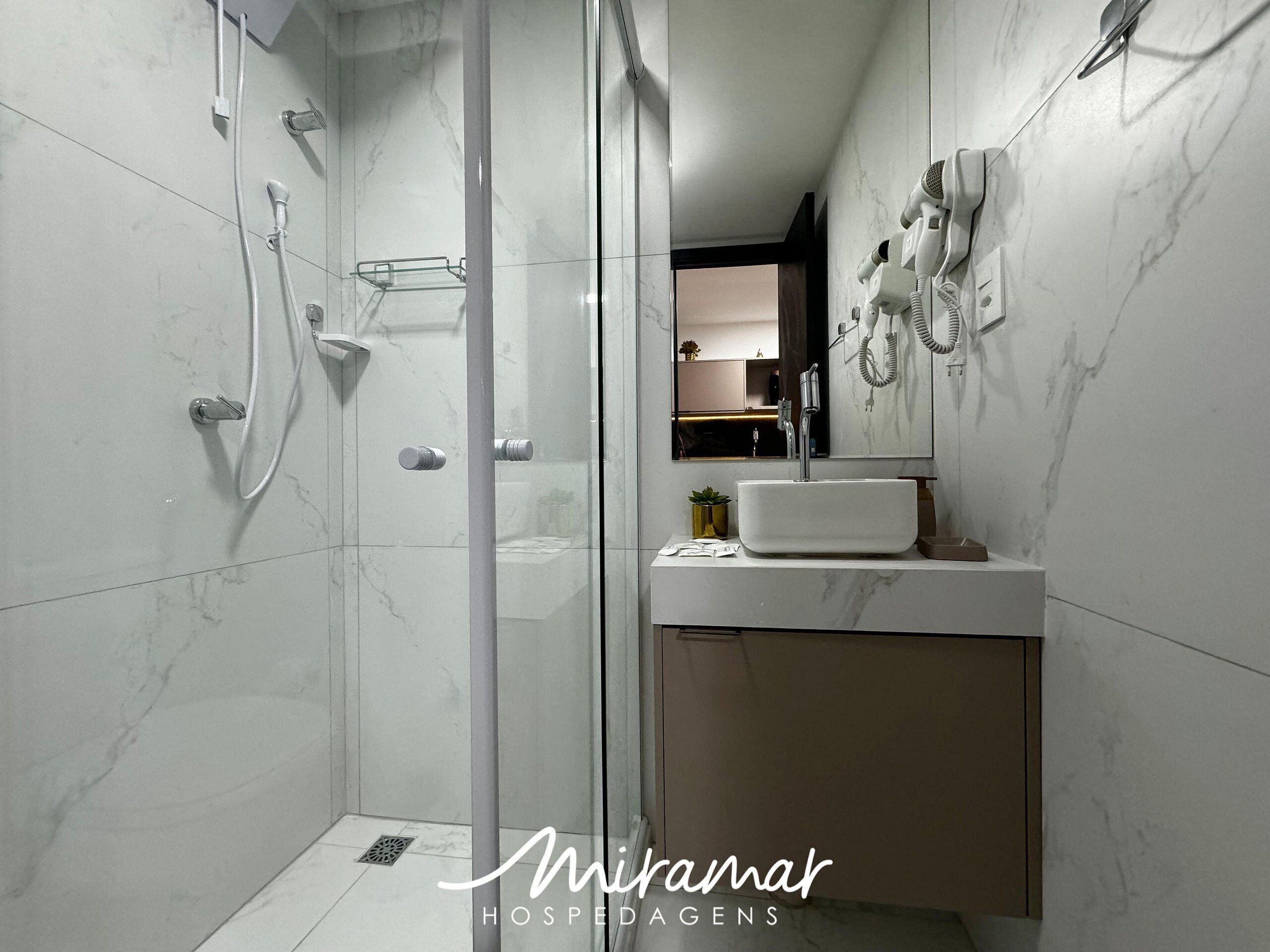 A modern bathroom with a glass shower enclosure, a white sink, and a hairdryer mounted on the wall.