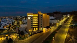 A multi-story hotel with a prominent sign, surrounded by a well-lit urban area with roads and other buildings. - Ankara Pedregal Centro de Convenciones (San Luis Potosi)