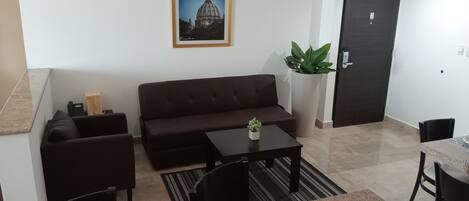 A living room with a brown sofa, a small table, a potted plant, and a framed picture on the wall.