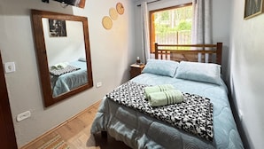 Een slaapkamer met een bed, een aan de muur bevestigde televisie, een raam met gordijnen en een spiegel.