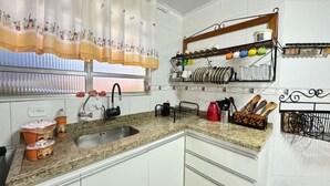 Een keuken met een granieten aanrechtblad, witte kasten, een roestvrijstalen spoelbak en een raam met bloemen gordijnen.