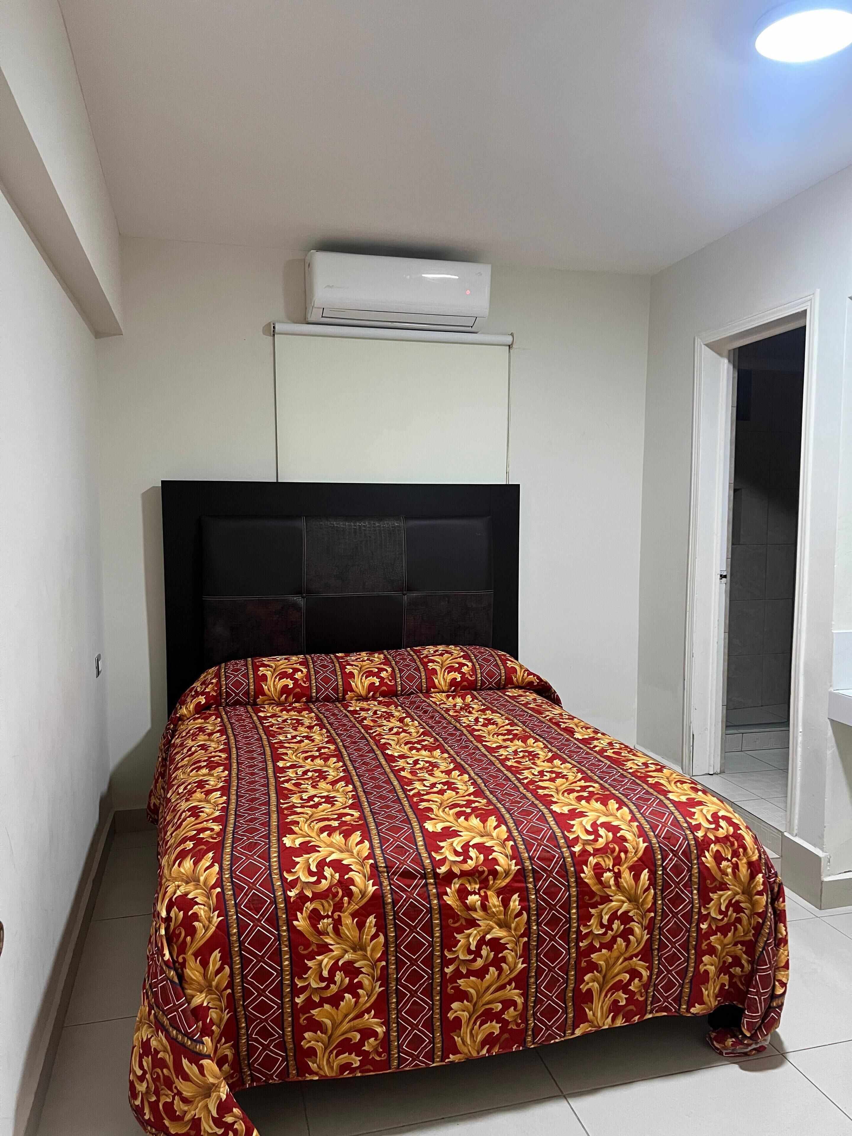 Un dormitorio con cama, aire acondicionado y puerta que da a un baño.
