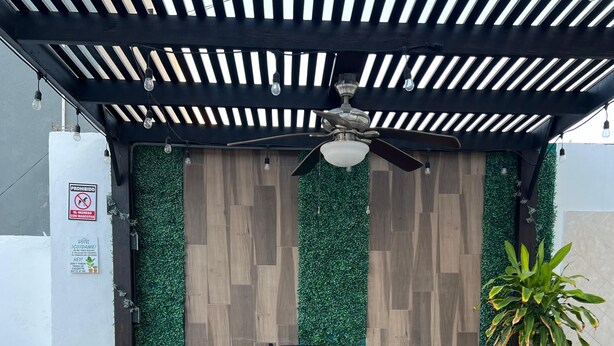 Une terrasse extérieure avec une table ronde et quatre chaises, un ventilateur de plafond et une plante en pot.