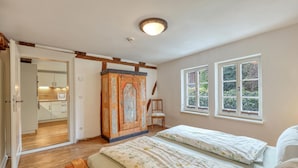 Un dormitorio con una cama de madera, una mesita de noche y vistas al jardín a través de dos ventanas.