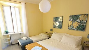 A hotel room with two beds, a wooden bench, a desk, a radiator, and two wall-mounted paintings. - Your window on Varenna-Como-. (Varenna)