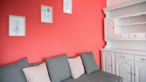 A room with a red wall, a grey sofa with cushions, and a white cabinet with drawers. - Your window on Varenna-Como-. (Varenna)