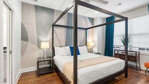 Un lit à baldaquin avec un cadre sombre, une table de chevet avec une lampe, un bureau avec une chaise et une fenêtre avec des rideaux.