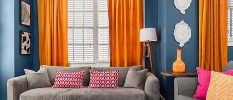 Un salón con un sofá gris, cortinas naranjas y una lámpara.
