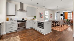 Une cuisine moderne avec des meubles blancs, une cuisinière, un four et un coin repas comprenant une table et des chaises.