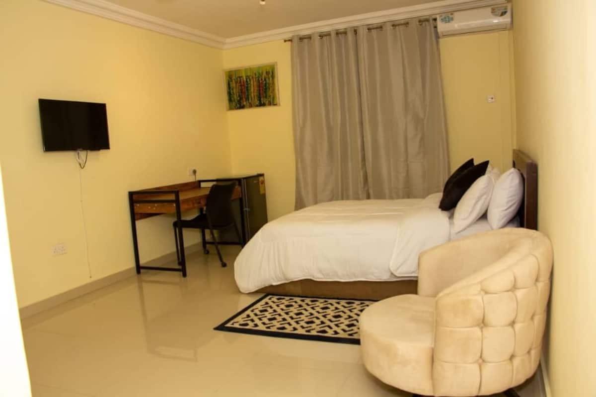 Une chambre à coucher avec un lit, un bureau, une chaise, un téléviseur et une fenêtre avec des rideaux.