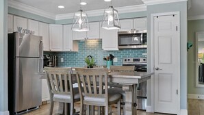 A kitchen with white cabinets, a stainless steel refrigerator, a microwave, and a stove. There are two wooden chairs and a small table. - Remodeled Waterfront Home with Heated Pool (New Port Richey)