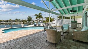 A covered outdoor area with a pool, wicker furniture, and a grill. - Remodeled Waterfront Home with Heated Pool (New Port Richey)