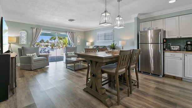 A modern kitchen with a dining area, a refrigerator, and a view of the outdoors. - Remodeled Waterfront Home with Heated Pool (New Port Richey)
