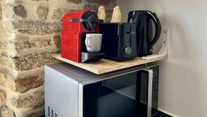 Ett kompakt kök med en vägg av sten, en röd kaffemaskin, en svart brödrost, en vit mugg och en svart kaffebryggare på en bänkskiva.