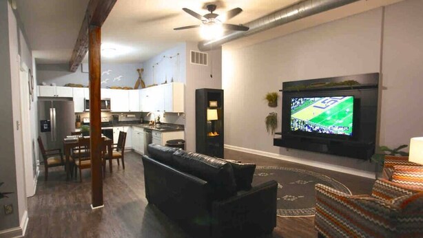 Una sala de estar moderna con un sofá de cuero negro, un tapete estampado y un televisor de pantalla plana montado en la pared.