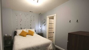 Un dormitorio con cama, mesita de noche, lámpara de pared y una puerta con cortina a rayas.