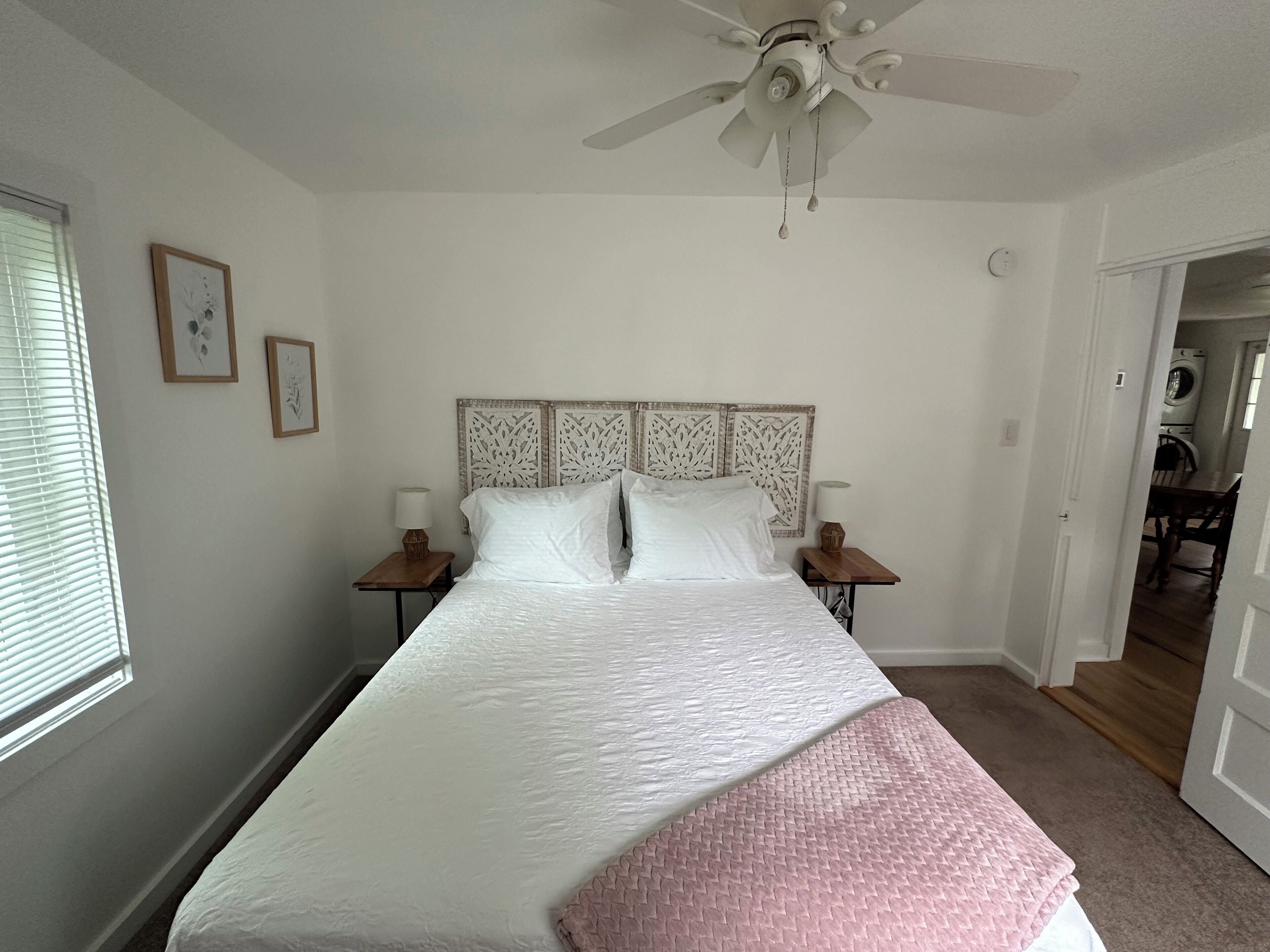 Un dormitorio con una cama, dos mesitas de noche, un ventilador de techo y una puerta que da a un área de lavandería.