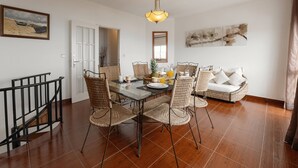 Uma área de refeições com mesa de vidro, cadeiras de vime e luminária pendente.