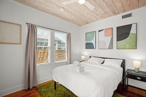 Ein modernes Schlafzimmer mit Holzboden, einem großen Bett mit weißer Bettwäsche, zwei Nachttischlampen und abstrakter Wandkunst.