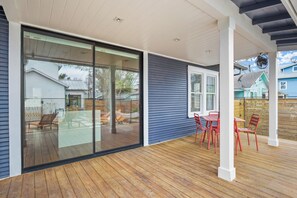 Eine überdachte Terrasse mit Holzdeck, einer Glastür zum Verschieben und roter Gartenmöbel.